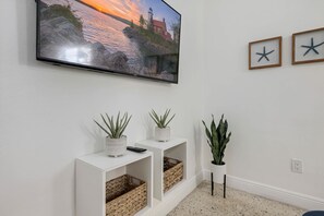 A living room with a flat-screen TV mounted on the wall, two potted plants on side tables, and a framed starfish decoration. - GROVE27-02 | soothing vibes near chic neighborhood (Miami)