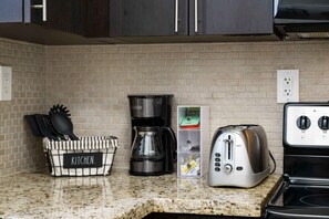 A kitchen with a granite countertop, a coffee maker, a toaster, and a basket labeled 'KITCHEN.'