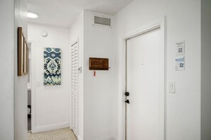 Un pasillo con una puerta blanca, un perchero, un aplique de pared y una obra de arte con motivos.