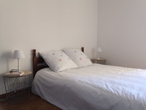 A neatly made bed with white bedding and decorative pillows, two bedside tables with lamps, and a wooden headboard. - Appartement T2, VUE Mer, 4 Personnes (L'ILE ROUSSE)