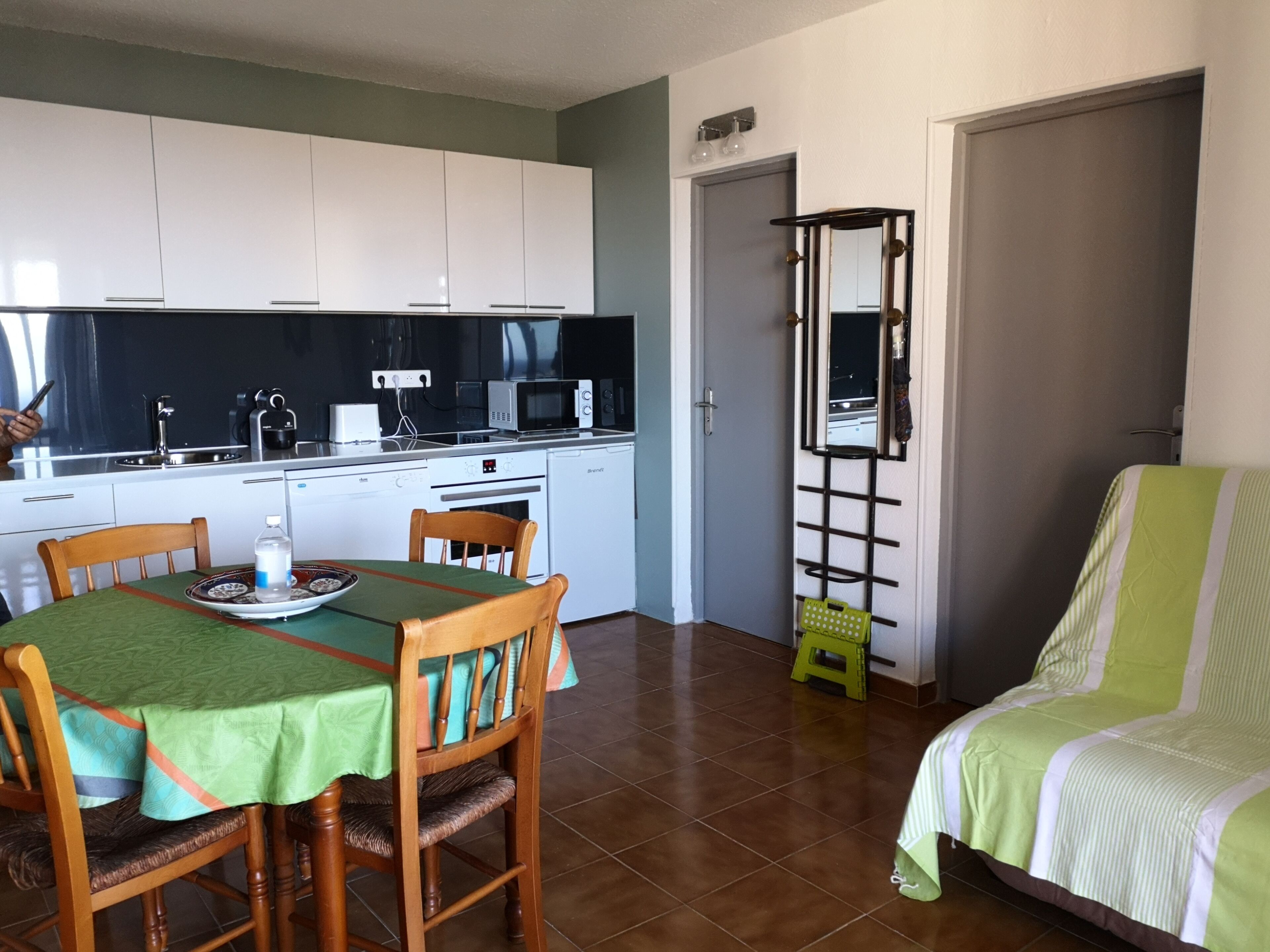 Une cuisine de taille réduite avec des meubles blancs, une table à manger avec des chaises, un four à micro-ondes et un évier.