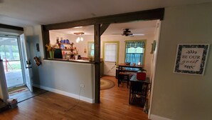 Un interior de vivienda con cocina, comedor y sala de estar. Hay piso de madera, una mesa de comedor con sillas, mostrador de cocina y un ventilador de techo.