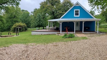 Charming house surrounded by lush greenery, featuring a covered porch with seating for relaxation.