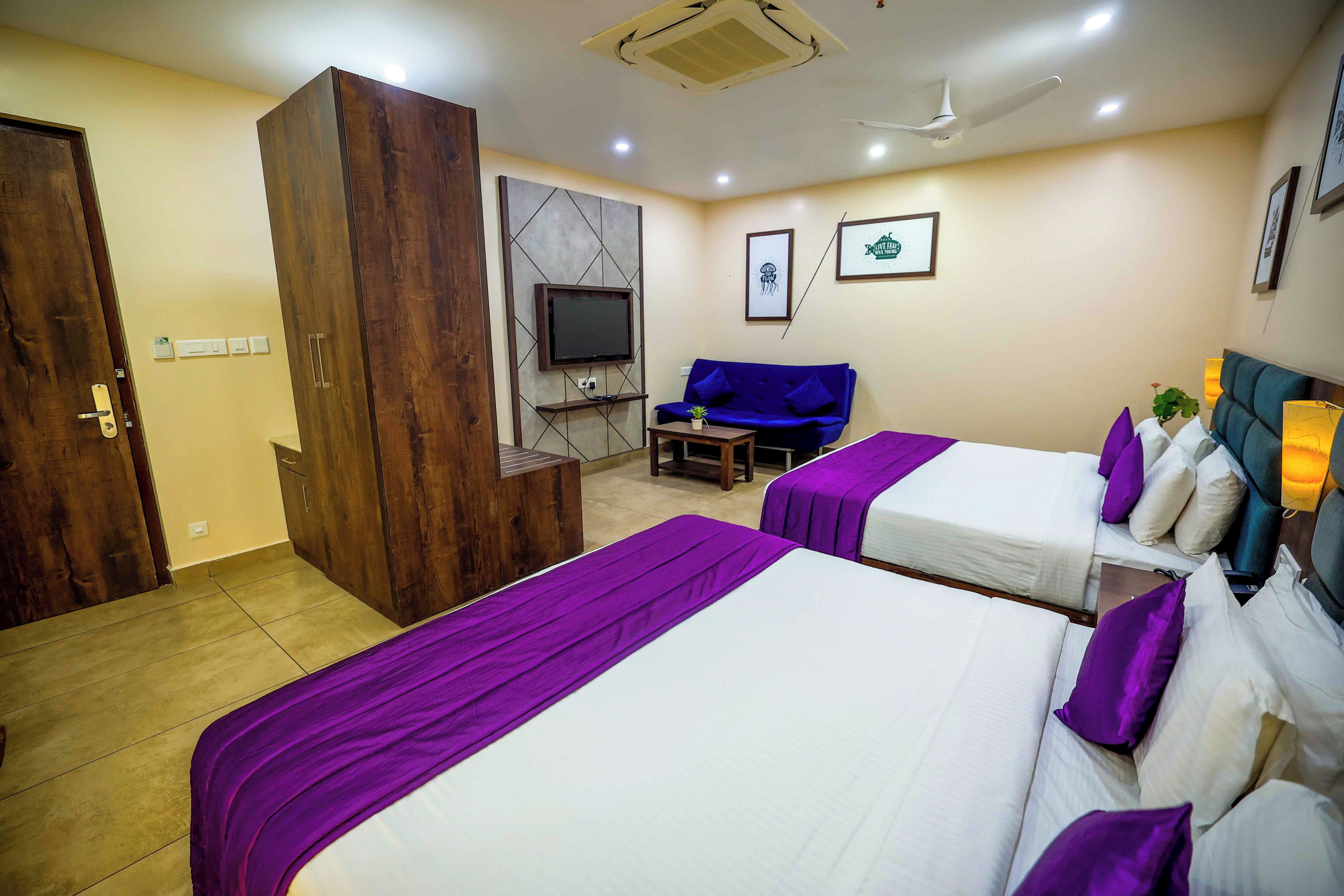 Quarto de hotel com duas camas, um sofá, uma televisão e um guarda-roupa.