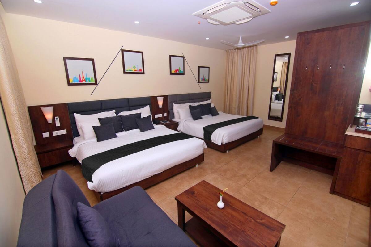 A hotel room with two beds, a sofa, a wooden table, and a mirror.