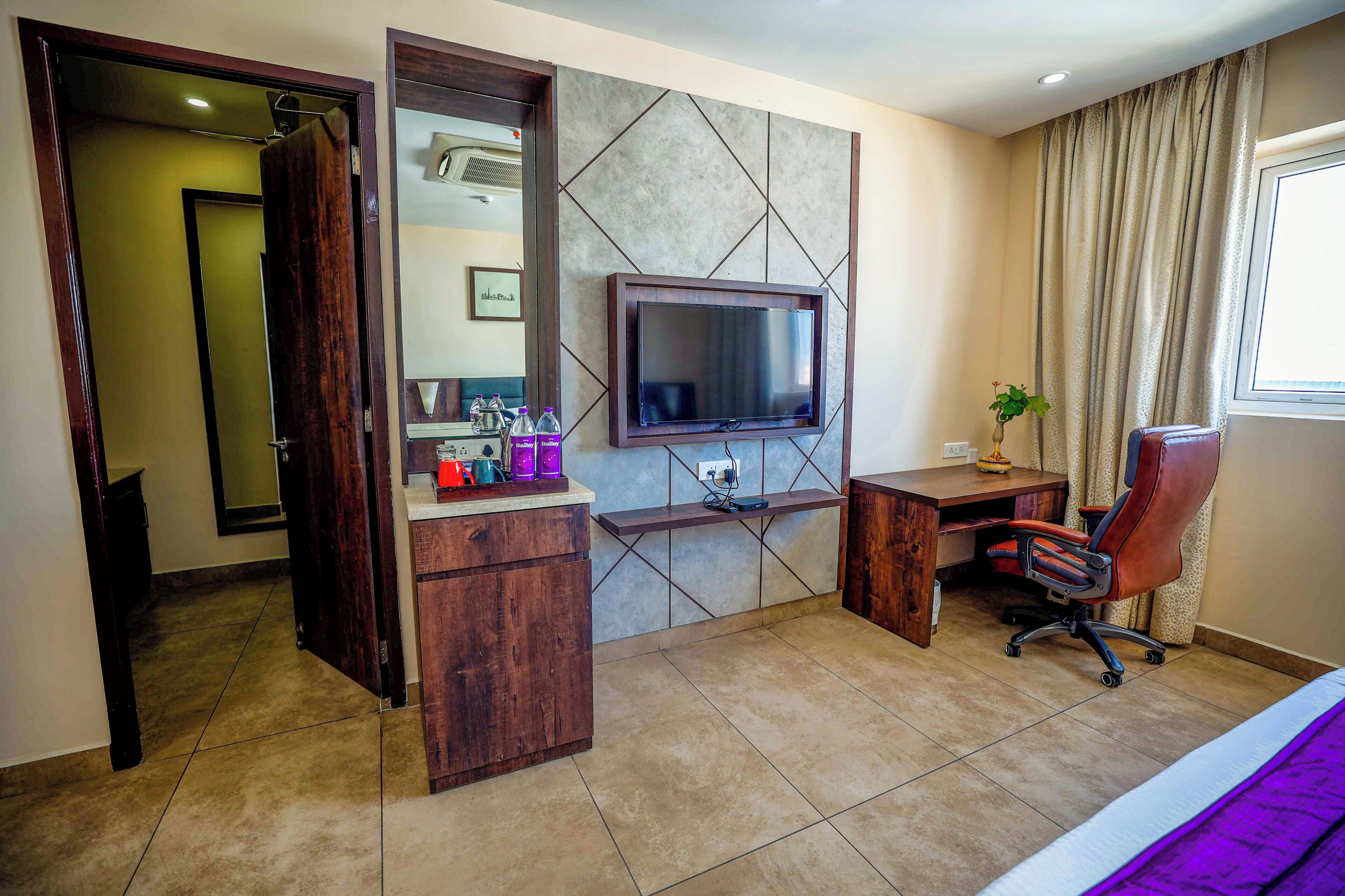 A hotel room with a bed, a desk, a chair, a television, a mirror, and a bathroom.