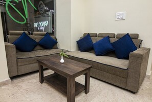 Una sala de estar con dos sofás grises, cada uno con cojines azules, una mesa de centro de madera y un jarrón con una planta.