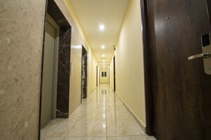 Un pasillo largo y estrecho con paredes de mármol y suelo de baldosas, que conduce a una puerta de madera oscura al final.