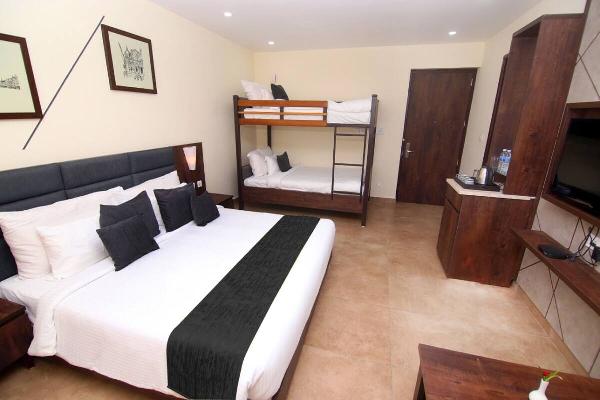 A hotel room with a large bed, a bunk bed, a TV, a wooden cabinet, and framed pictures on the wall.