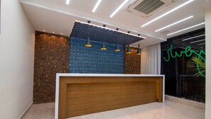 Un área de recepción con un mostrador de madera, pared con textura, iluminación colgante y un letrero de neón.