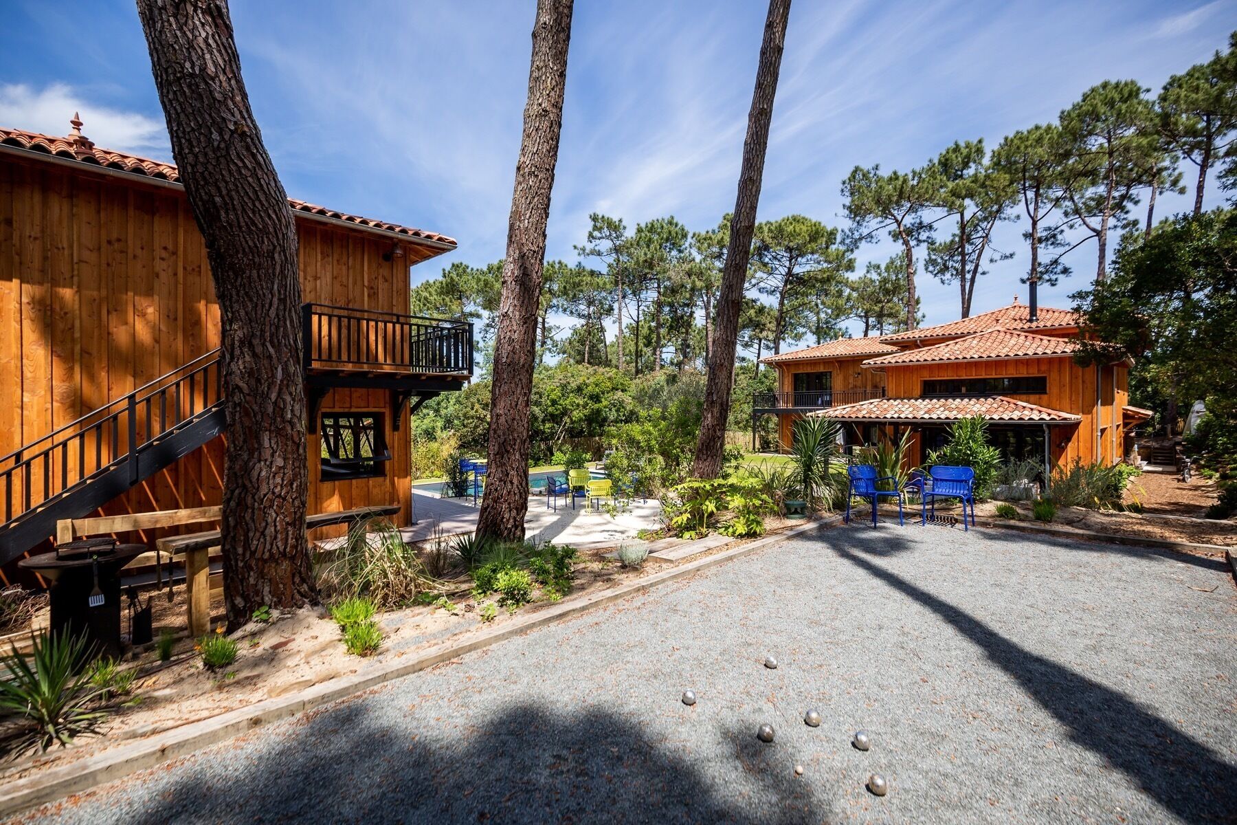 Un chalet rustique en bois, doté d’un balcon, entouré de grands pins et accessible par une allée de gravier.
