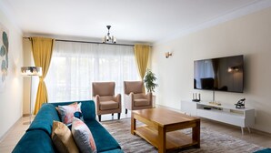 A modern living room with a teal sofa, two beige armchairs, a wooden coffee table, and a flat-screen TV on a white stand. - Casa Misa Westlands (Nairobi)