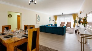 A dining area with a wooden table set for six, a blue sofa, and a kitchen area in the background. - Casa Misa Westlands (Nairobi)