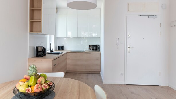Une cuisine moderne avec des meubles en bois, une porte blanche et un panier de fruits sur la table.