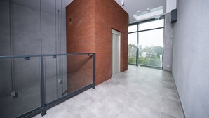 Un couloir moderne avec une porte en verre donnant sur un balcon, une rambarde en métal et une vue sur l’extérieur.