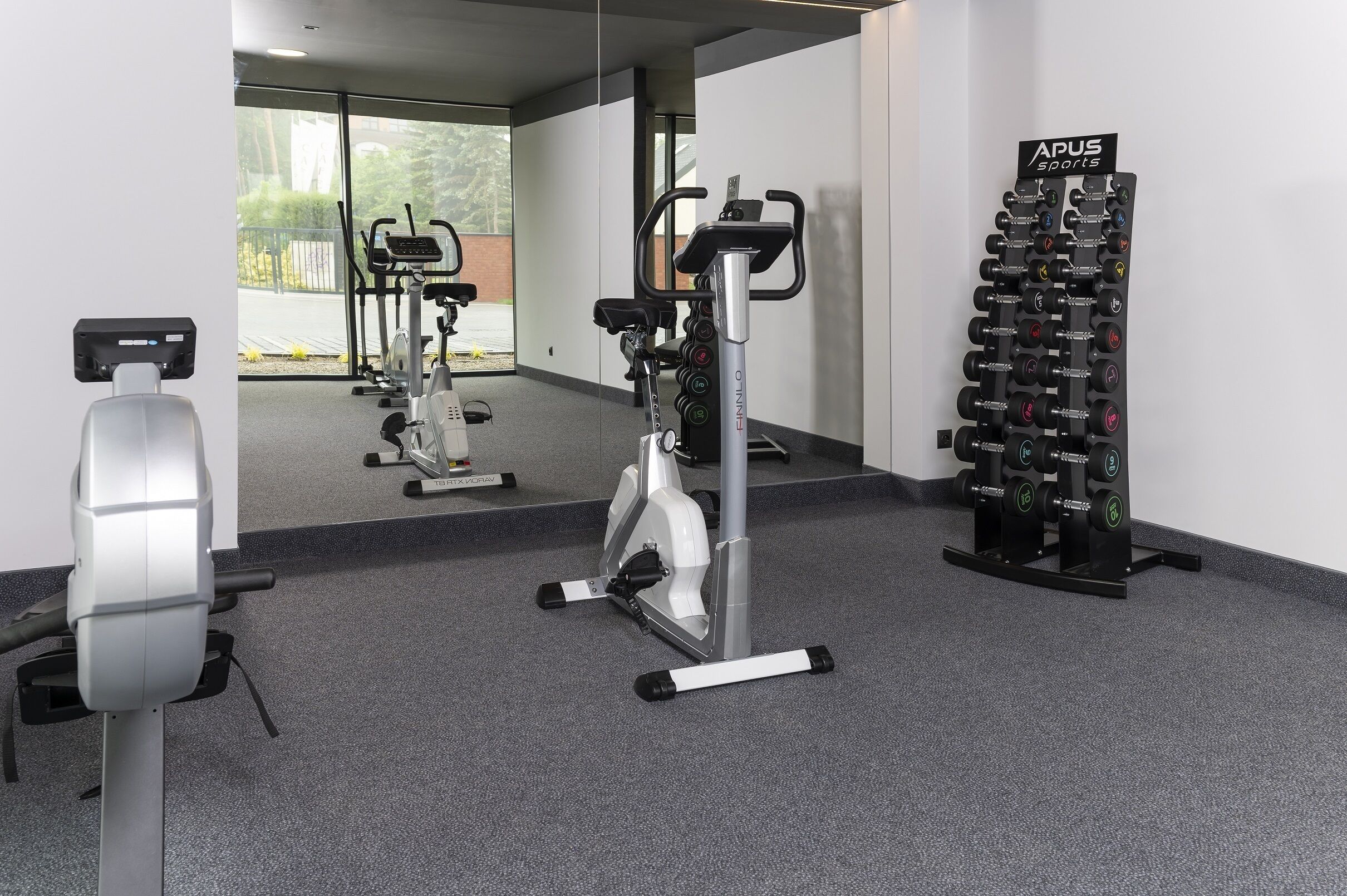 Un gimnasio con máquinas de cardio, equipo de levantamiento de pesas y un espejo que refleja el espacio.
