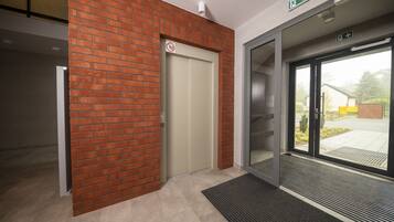 Un ascensor moderno con pared de ladrillo rojo, puerta de cristal y un cartel de prohibido fumar sobre la puerta.