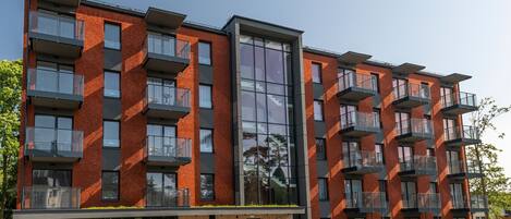 A modern multi-story building with a brick facade, large windows, and balconies.