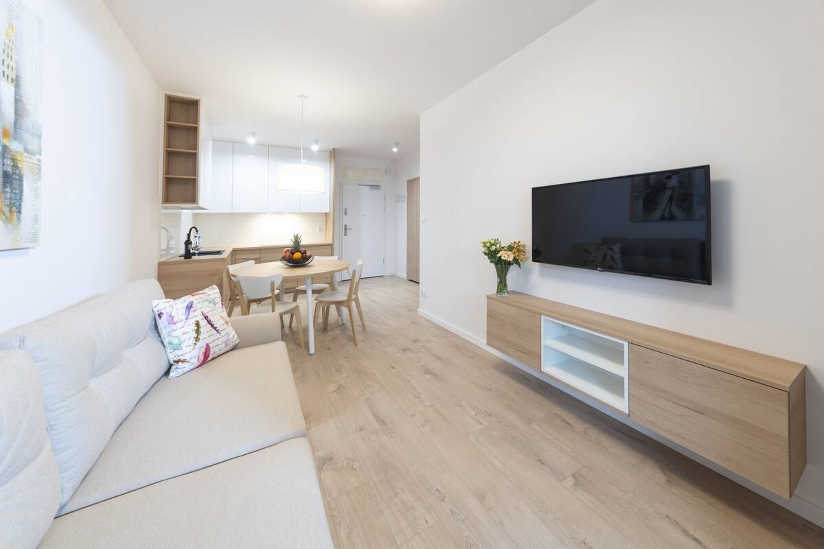 Una sala de estar moderna con un sofá, televisor y un comedor con sillas y una mesa.