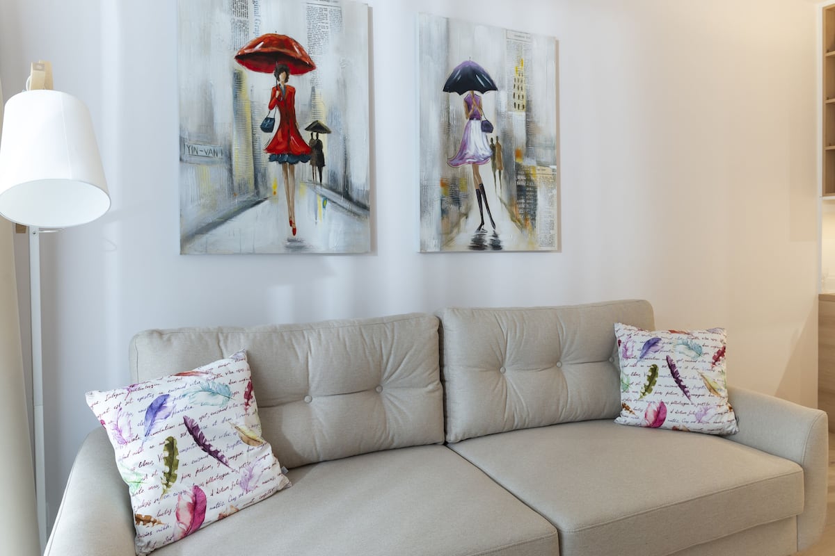 Una sala de estar moderna con un sofá beige, dos cojines decorativos y dos cuadros abstractos en la pared.