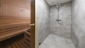 Un sauna avec des bancs en bois et un espace douche aux carreaux gris.