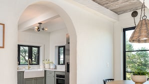 Una cocina moderna con un arco que da a una zona de comedor, suelo de madera y una lámpara colgante.