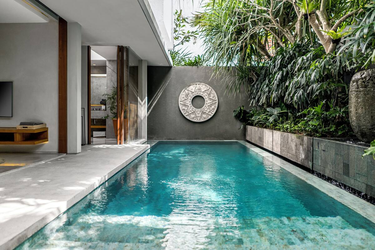A modern indoor pool with a clear blue water surface, surrounded by a concrete wall with a decorative metal plate.