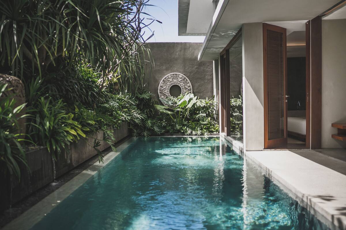 A swimming pool with a circular decorative wall, surrounded by lush greenery and modern architecture.
