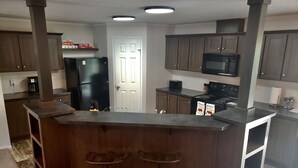 A modern kitchen with a central island, bar stools, a refrigerator, microwave, stove, and wooden cabinets. - Secluded in the woods. No neighbors in sight. (Pullman)