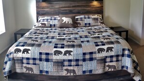 A bedroom with a bed featuring a quilted bedspread with bear patterns, a wooden headboard, bedside lamps, and a motivational quote on the wall. - Secluded in the woods. No neighbors in sight. (Pullman)