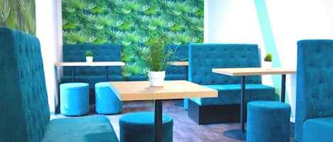 Un área de estar moderna con asientos tapizados en color aguamarina, una mesa de madera y un mural de pared con motivos vegetales.
