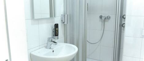 A bathroom with a white sink, a handheld showerhead, and a glass-enclosed shower.