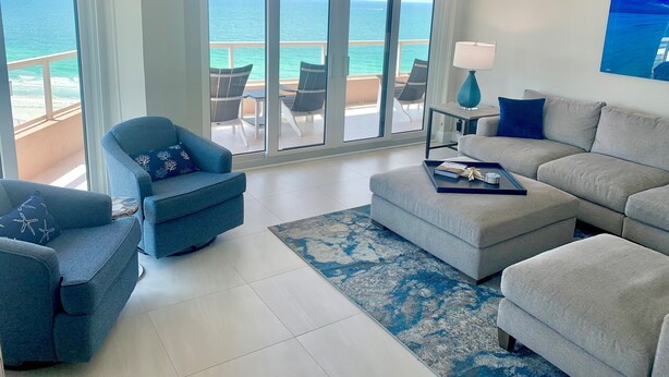 Un salón con vista al océano, un sofá, un sillón y una mesa de centro.