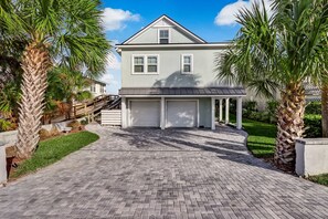 A two-story house with a garage, surrounded by a paved driveway and palm trees.
