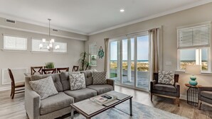 A spacious living room with a grey sofa, a coffee table, and a view of the beach through large windows. - Pet friendly, newly renovated, ocean and beachfront historical home (Fernandina Beach)