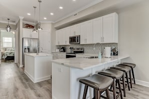 A modern kitchen with white cabinetry, stainless steel appliances, and a central island with bar stools.