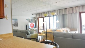Habitación de hotel con zona de comedor, sofá, televisor y ventana con cortinas.