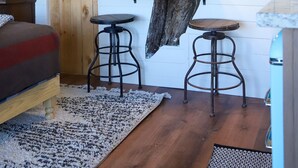 Une pièce chaleureuse avec un plancher en bois, un lit, une petite table et un luminaire suspendu.