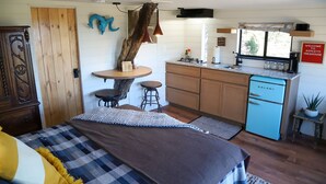 Une chambre à coucher de taille réduite, comprenant un lit, des tables de chevet et un petit coin salon avec une table et des tabourets.