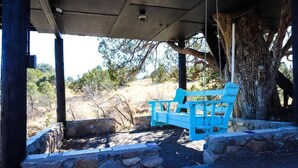 Un espace extérieur abrité, aménagé avec un banc bleu, des murs en pierre et le tronc d’un arbre.