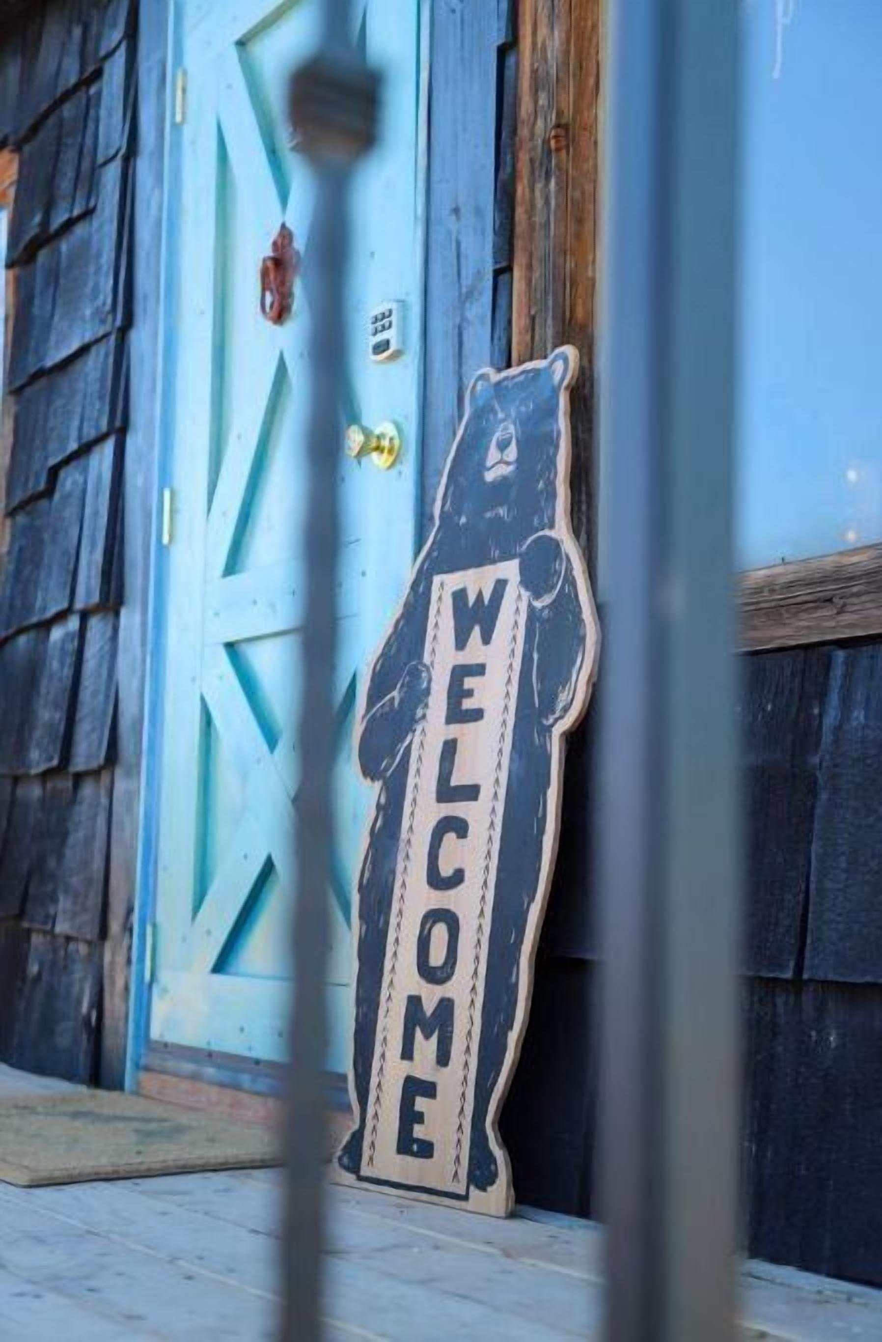Une porte en bois ornée d’un motif géométrique bleu et d’une enseigne en forme d’ours sur laquelle on peut lire « BIENVENUE ».