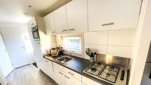 Una cocina moderna con gabinetes blancos, una estufa a gas, un lavamanos y una ventana con persianas.