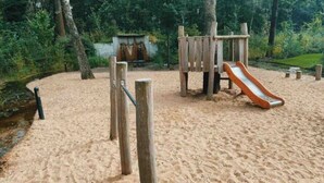 Un parque infantil de arena con un tobogán y estructuras de madera para escalar.