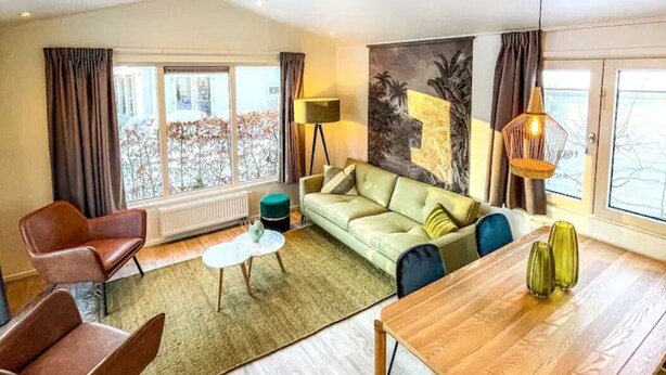 Una sala de estar moderna con un sofá, sillas, una mesa de comedor y un gran ventanal con cortinas.
