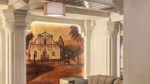 Un hall d’entrée orné d’une fresque représentant un bâtiment colonial, doté d’un sol à carreaux et comprenant un espace détente avec un canapé et un pouf.