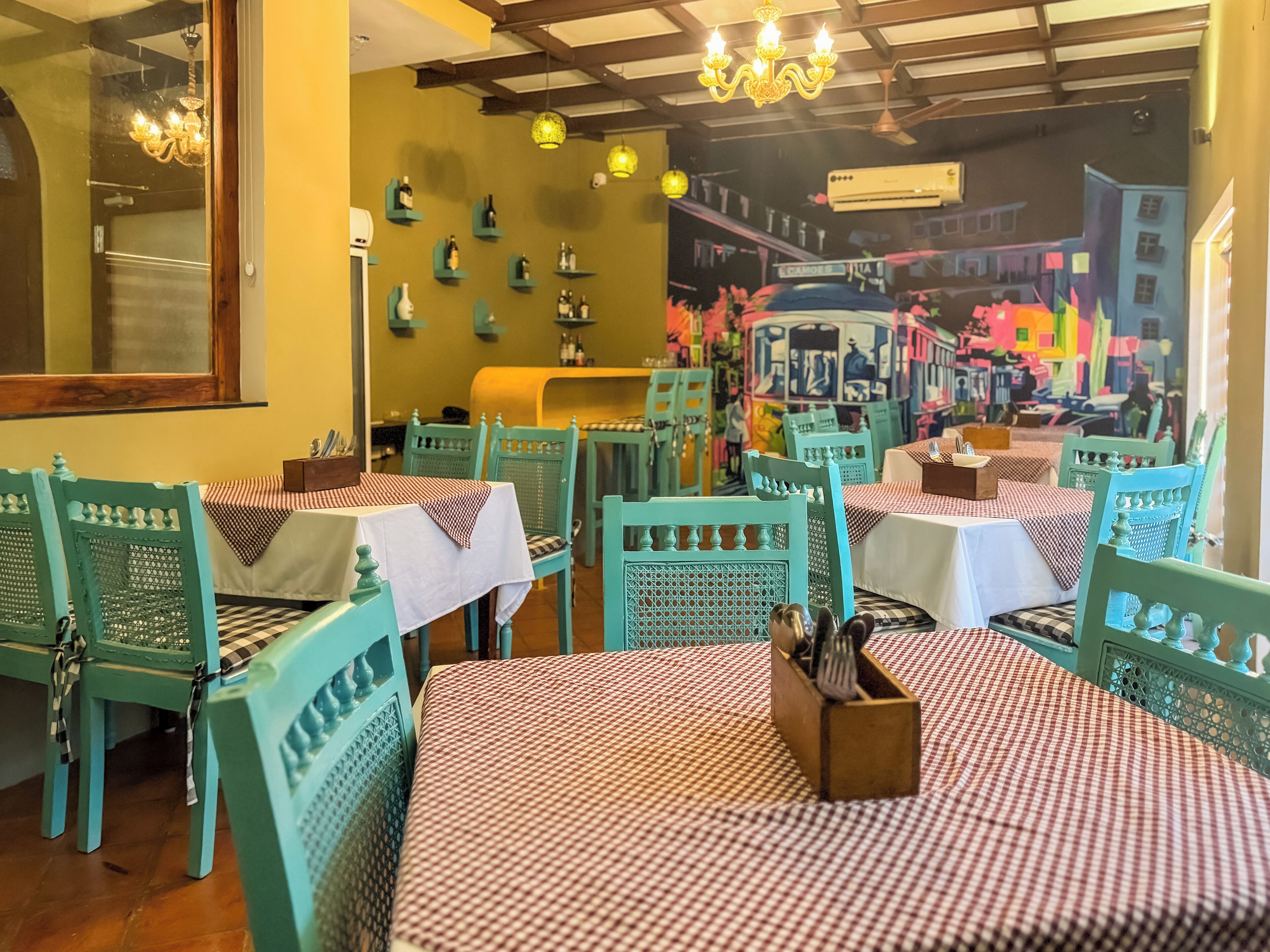A restaurant with teal chairs and checkered tablecloths, featuring a mural of a cityscape on the back wall.
