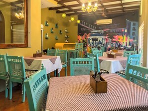 A restaurant with teal chairs and checkered tablecloths, featuring a mural of a cityscape on the back wall. - Le Chateau (Puducherry)