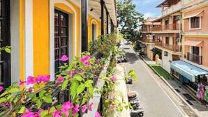 Une rangée de bâtiments jaunes et blancs dotés de balcons, une rue qui les sépare, et quelques espaces verts.