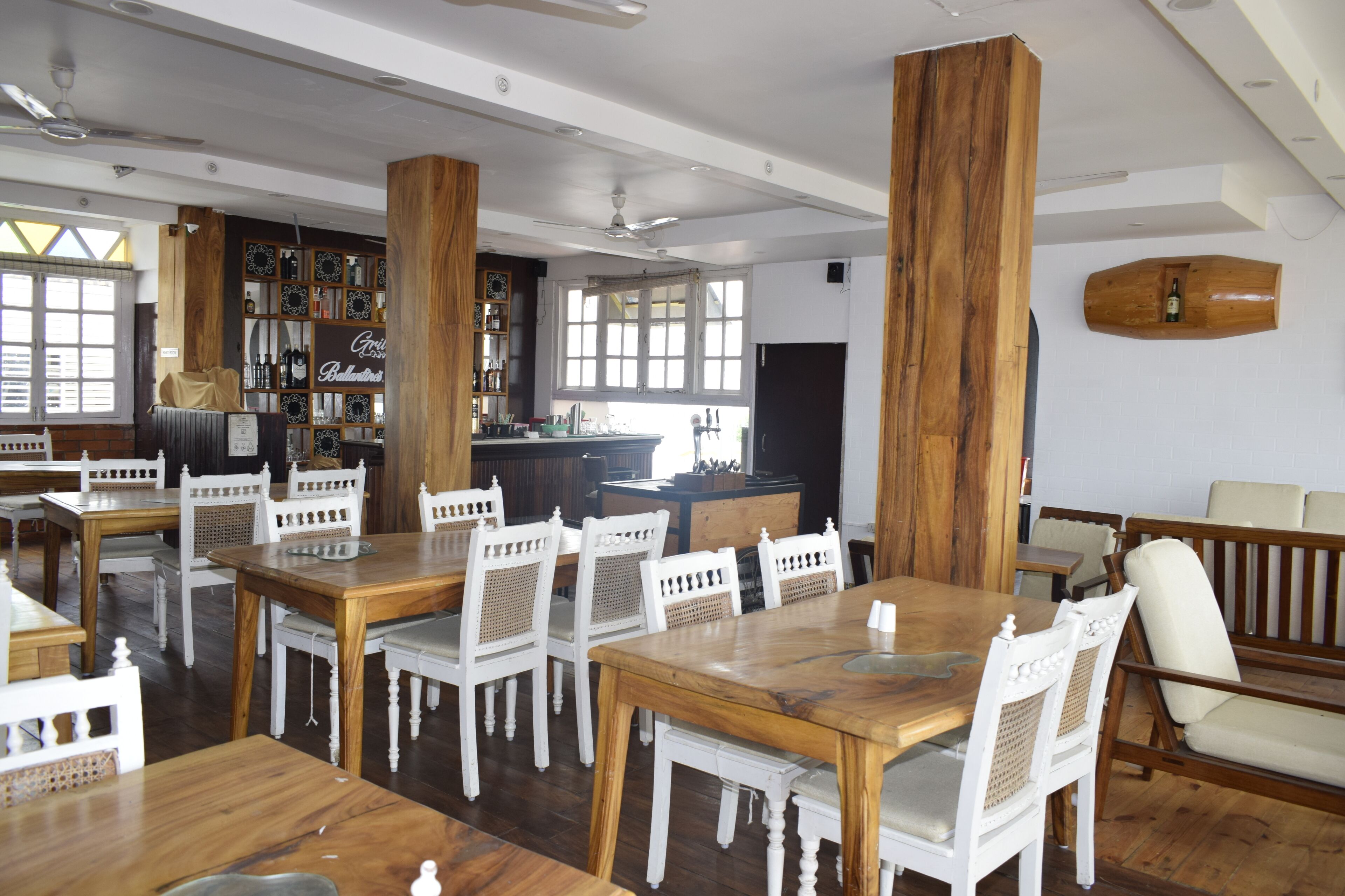 A spacious dining area with wooden tables and white chairs, a bar area, and a bookshelf with various items.