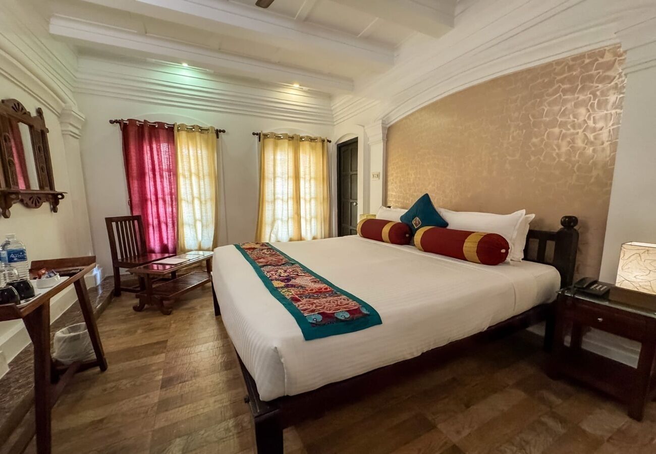 A hotel room with a large bed, wooden floor, a desk with a chair, and a nightstand.